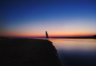 Silhouette man walking on beach against clear sky