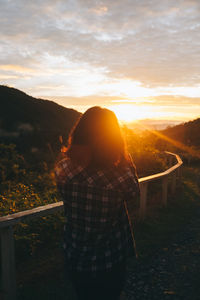 Rear view of woman on landscape against sunset sky