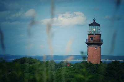 Lighthouse by trees and mountain against sky