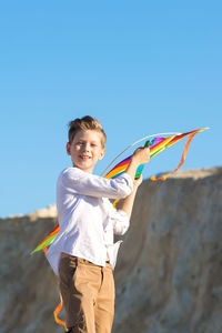 A boy in a white shirt with a kite in his hands plays in the mountains.