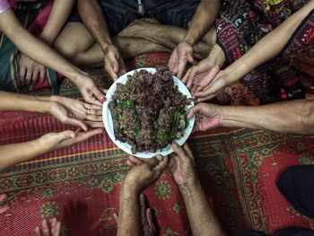 Low section of friends holding food in plate on carpet