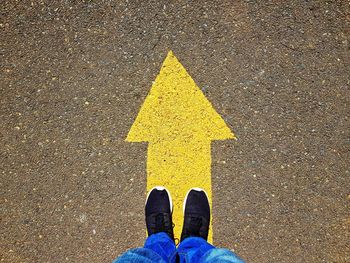 Low section of man standing on arrow sign at road