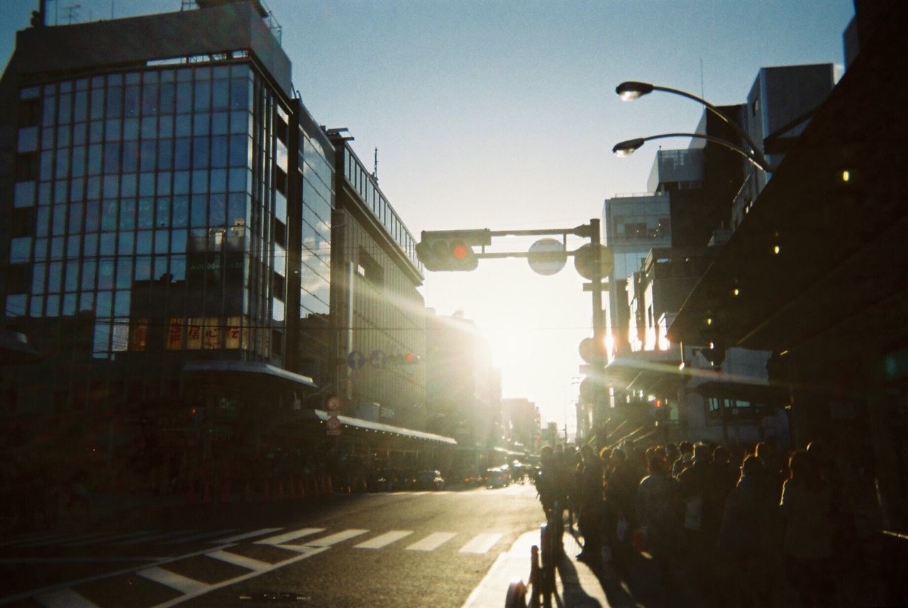 building exterior, architecture, built structure, street, city, transportation, car, the way forward, road, sunlight, city street, city life, clear sky, sky, street light, sun, building, lens flare, land vehicle, sunbeam