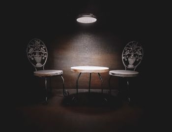 Empty chairs and table against wall in dark room