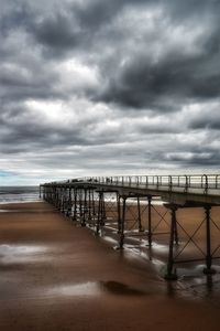 View of pier on beach against cloudy sky