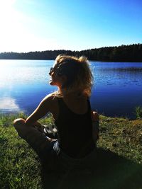 Woman sitting by lake against sky