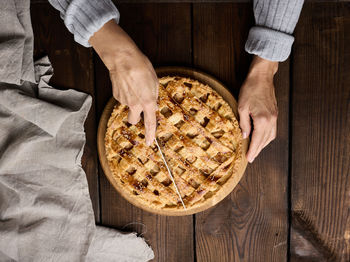 A woman cuts a baked round pie with apples with a knife on a wooden table, view of the top