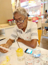 Senior man looking at paper while sitting on table at restaurant