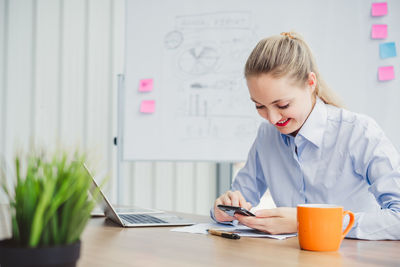 Smiling young businesswoman using phone on office desk