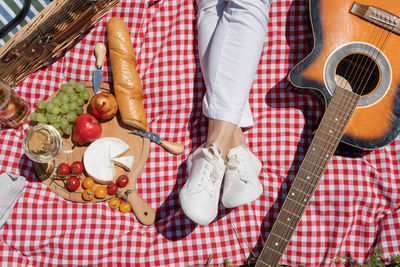 Top view of unrecognizable young woman in white pants outside having picnic, eating and playing gui