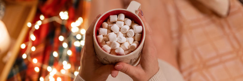 Cup of hot chocolate drink with marshmallows in female holding hands of woman in knitted sweater 