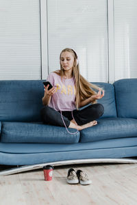 Full length of woman using mobile phone while sitting on sofa