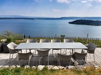 Chairs and table by lake against sky