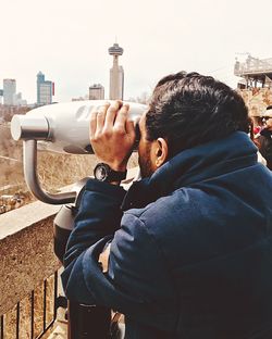 Man looking through coin-operated binoculars in city