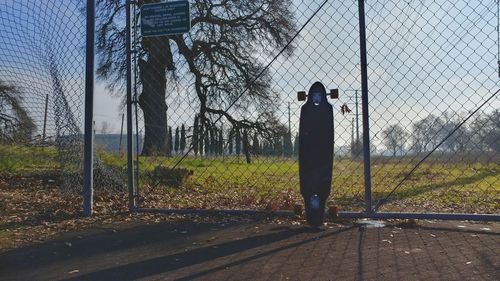 Rear view of man standing by chainlink fence against sky