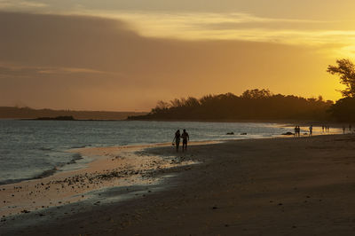 People on beach against sky during sunset