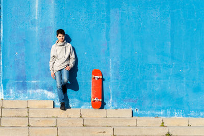 Young teen with hand on pocket standing against blue wall