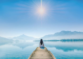 Rear view of woman on pier at lake against sky