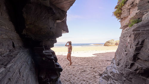 Woman on rock at beach against sky