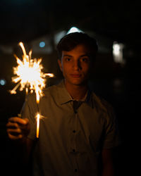 Portrait of young man holding illuminated sparkler at night