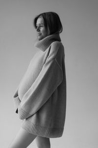 Young woman wearing sweater standing against wall