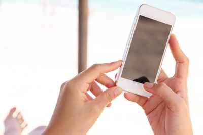 Close-up of man photographing through mobile phone against sky at beach