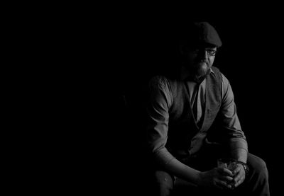 Portrait of man sitting against black background