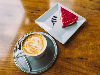 A cup of cappuccino and a piece of cheesecake on a wooden table.