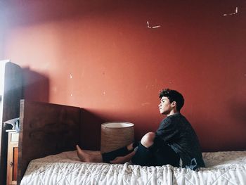 Side view of thoughtful man sitting on bed against wall