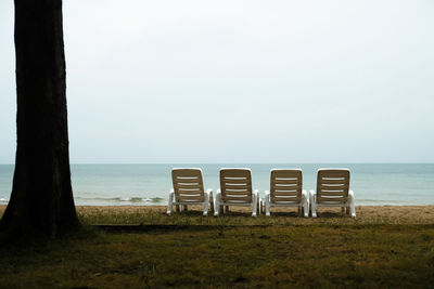 Empty chairs arranged on grassy field by sea against sky against sky