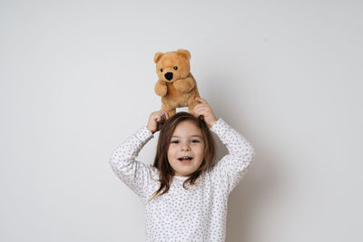 Portrait of cute girl with teddy bear against wall