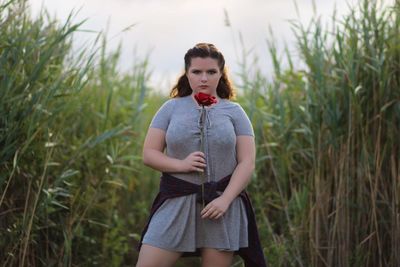 Portrait of overweight young woman holding rose while standing on field