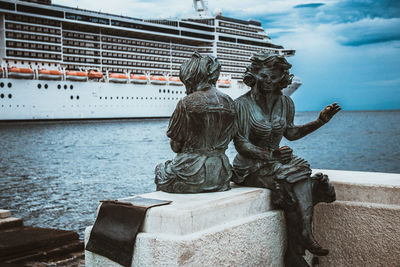 Statues in trieste near the sea against cloudy sky