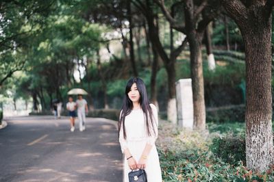 Full length of young woman standing against trees