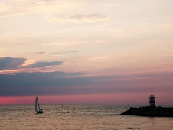 Lighthouse by sea against sky during sunset