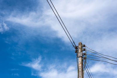 Low angle view of electricity pylon against cloudy blue sky