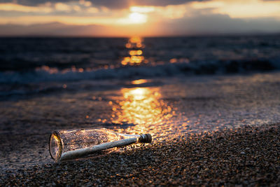 Message in a bottle on a beach at sunset against sky