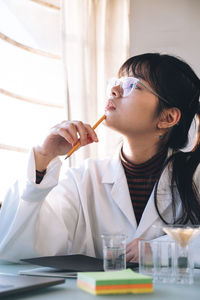 Contemplative chemist sitting at table with pen in laboratory