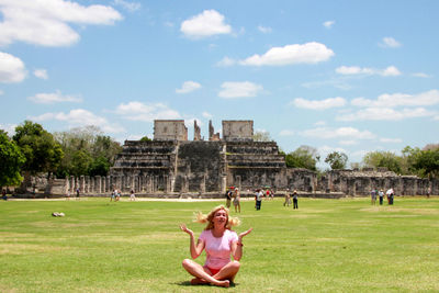 Woman sitting on grassy field against historical building