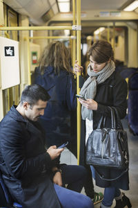 Male and female passengers using mobile phone in tram