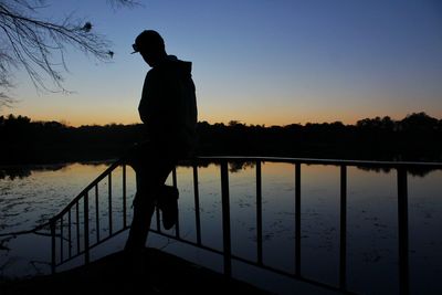 Silhouette man standing by lake against sky during sunset