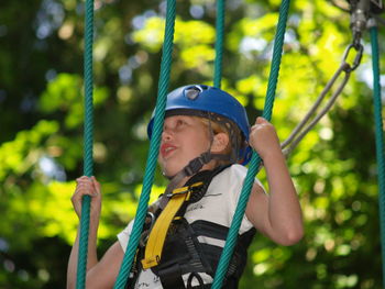 Low angle view of girl climbing on rope in forest