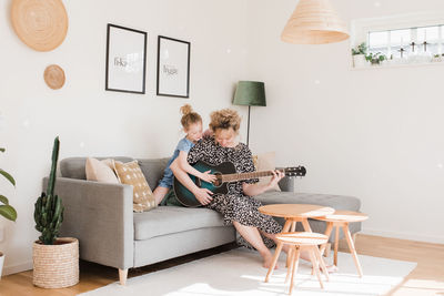Mother and daughter playing guitar together at home