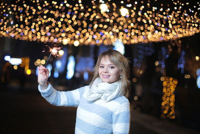 Portrait of smiling woman holding illuminated sparkler at night