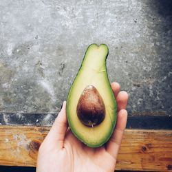 Cropped hand of woman holding avocado against wall