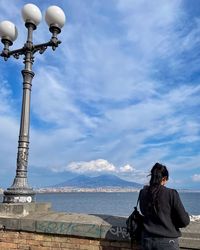 Rear view of woman standing by sea against sky