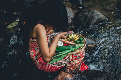 Young woman sitting with food on riverbank in forest
