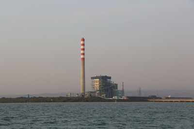 Lighthouse by sea against clear sky