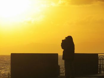 Silhouette of woman standing against sky at sunset