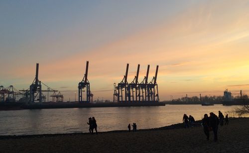 People at beach against harbor during sunset